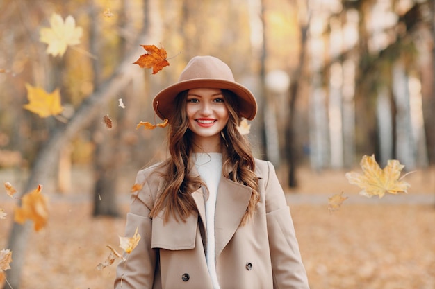 Bella ragazza sorridente al parco autunnale volante caduta foglie gialle del fogliame