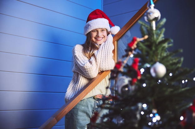 Bella ragazza sorridente che si rallegra del bellissimo albero di Natale