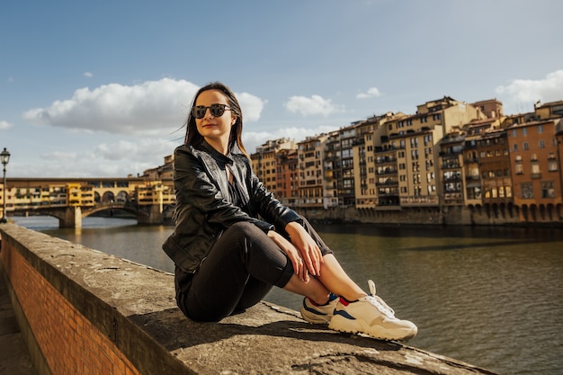 Bella ragazza sorridente con gli occhiali a Firenze con il ponte vecchio e il fiume Arno sullo sfondo.