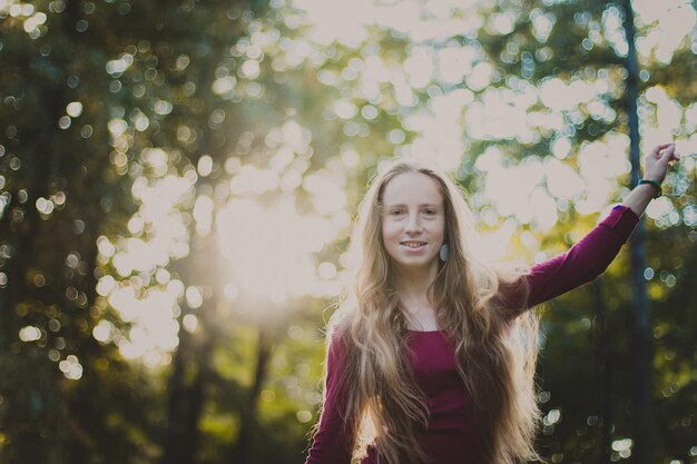 Bella ragazza sorridente con lunghi capelli biondi in una camicetta viola in piedi nel parco