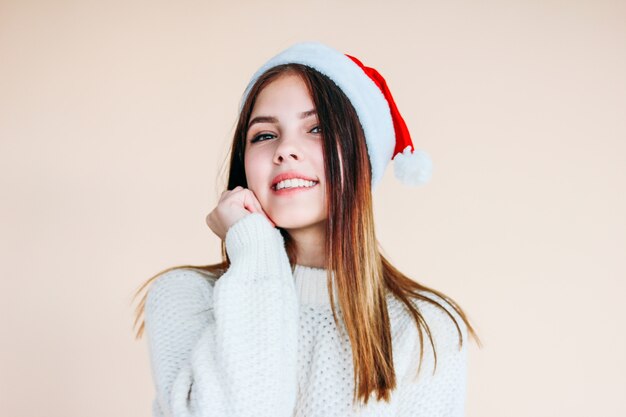 Bella ragazza sorridente con pelle pulita che indossa cappello santa e accogliente maglione bianco