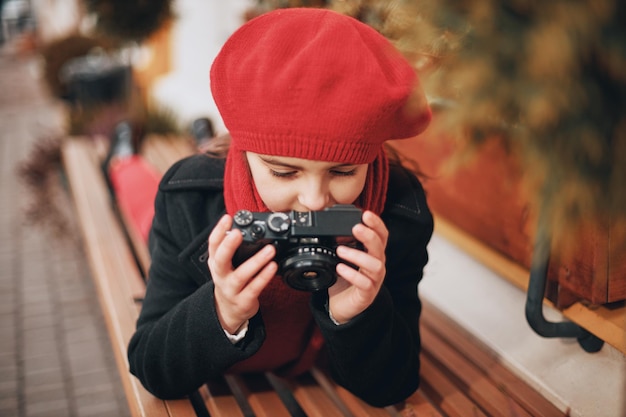 Bella ragazza sorridente con un berretto rosso e una sciarpa scatta foto sulla strada della città. Foto di alta qualità