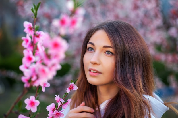 Bella ragazza sorridente in piedi vicino a un albero di pesco durante il tramonto. Faccia felice. Tempo di primavera.