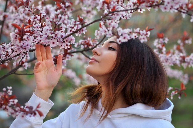 Bella ragazza sorridente in piedi vicino a un albero di pesco durante il tramonto Volto felice Tempo di primavera