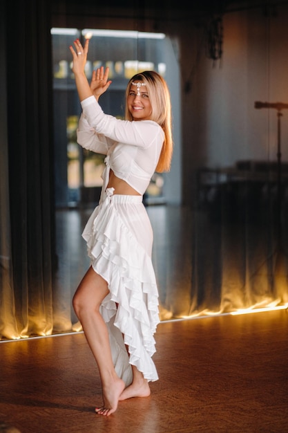 Bella ragazza sorridente in un vestito bianco che balla in palestra