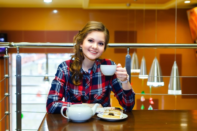 Bella ragazza sorridente in una camicia a quadri che beve tè in un caffè