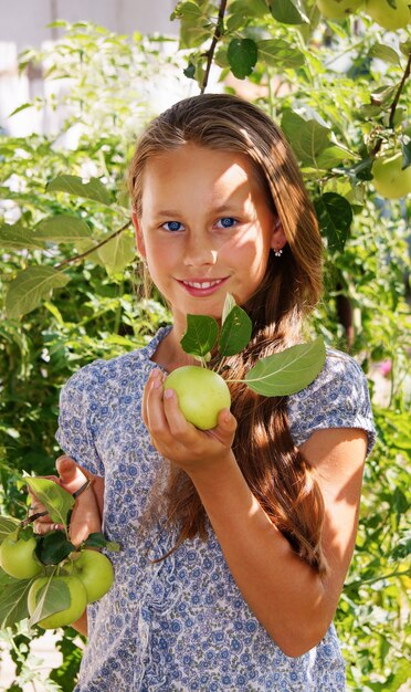 Bella ragazza sorridente nel giardino con mele verdi, vestito blu con fiori