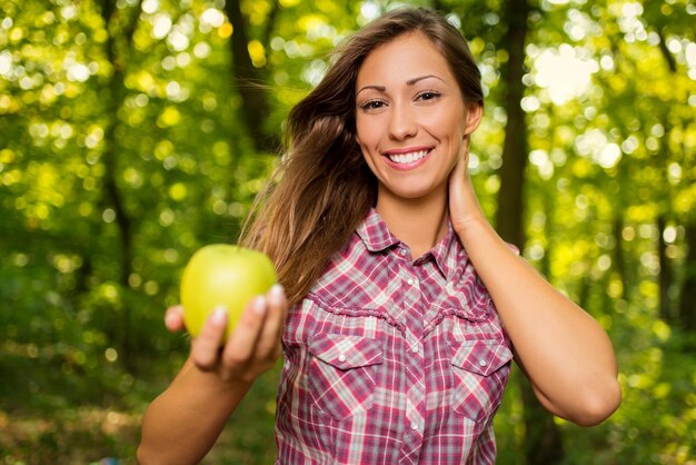 Bella ragazza sorridente nella natura che tiene mela verde e che guarda l'obbiettivo.