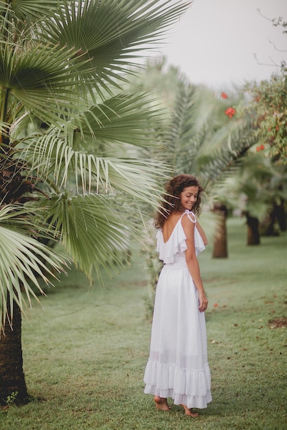 Bella ragazza sorridente vicino alle palme in un vestito bianco