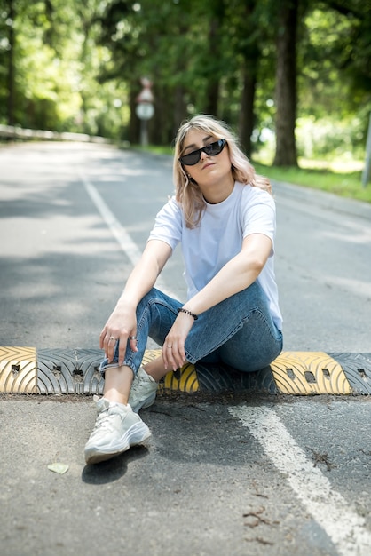 Bella ragazza sottile con indossare un panno casual seduto sulla strada nel bosco, giorno d'estate. all'aperto