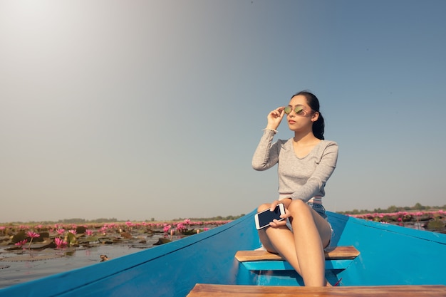 Bella ragazza sulla barca blu nel lago di loto rosa al mattino. Protezione solare.