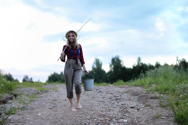 Bella ragazza sulla natura in riva al fiume con una canna da pesca