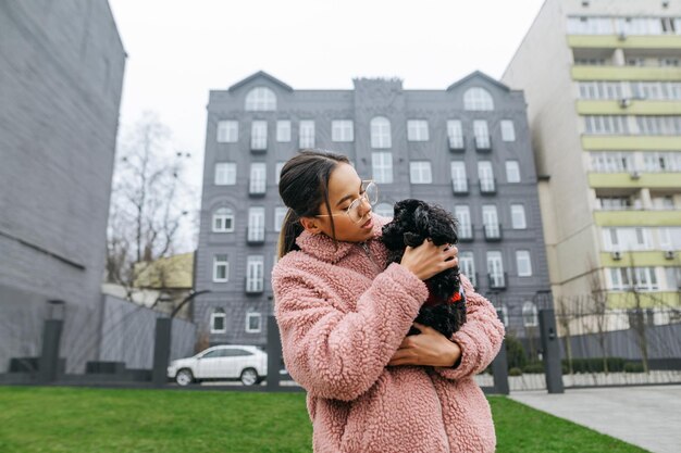 bella ragazza sulla strada della città che tiene in braccio un simpatico cagnolino e lo abbraccia