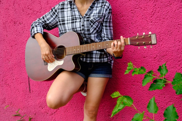 Bella ragazza suona la chitarra acustica Chitarrista su uno sfondo rosa Bella giovane acustica