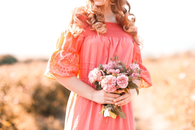 Bella ragazza teenager bionda che indossa un vestito rosa che tiene il fiore di rosa all'aperto