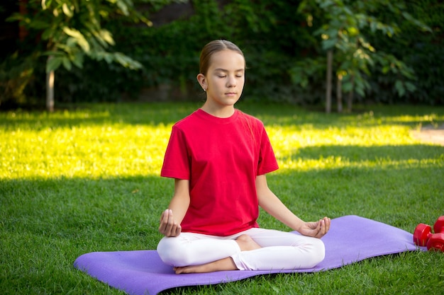 Bella ragazza teenager che pratica yoga sull'erba al parco