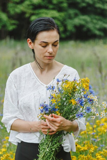 Bella ragazza tra il campo estivo con fiori di campo