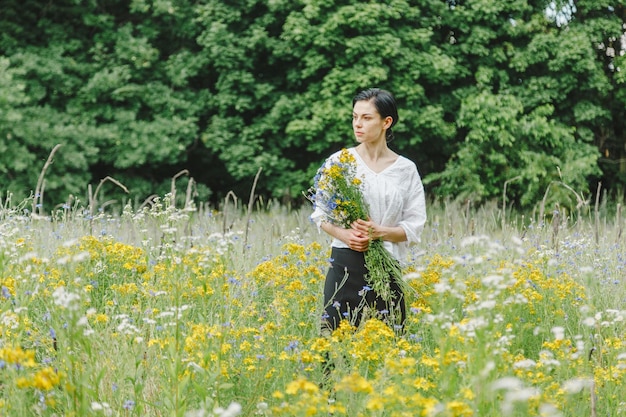 Bella ragazza tra il campo estivo con fiori di campo