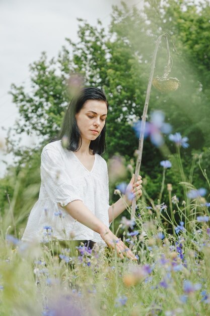 Bella ragazza tra il campo estivo con fiori selvatici in primo piano