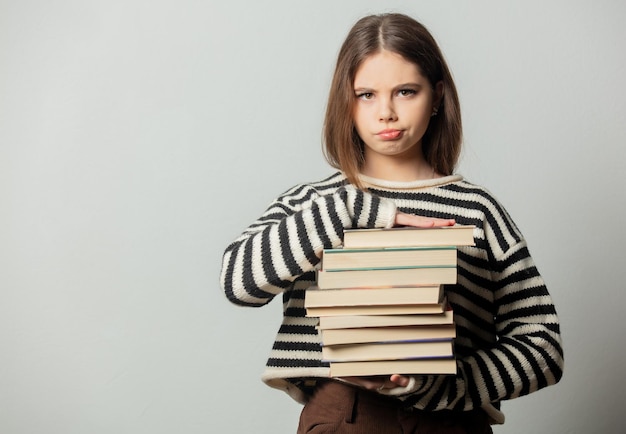 Bella ragazza triste in maglione a righe con libri su sfondo bianco