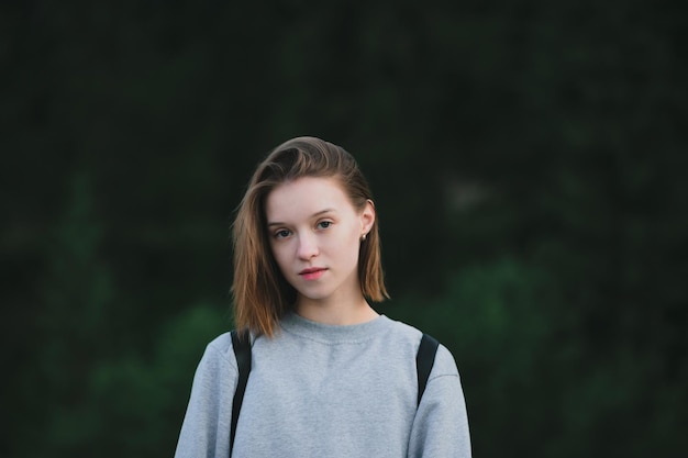 Bella ragazza turistica in maglione grigio in posa su sfondo sfocato foresta