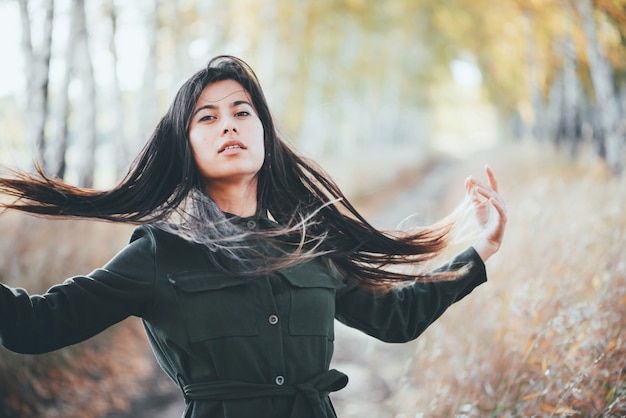 Bella ragazza vaga con capelli neri naturali lunghi sul fondo del bokeh delle foglie di giallo di autunno.