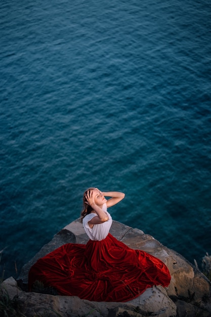 Bella ragazza vestita con un vestito rosso sullo sfondo del mare