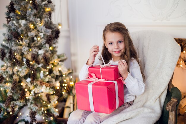 Bella ragazza vicino all'albero di Natale disimballaggio presenta seduto su una sedia