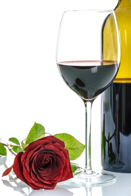 Bella rosa rossa e bicchiere di vino rosso e una bottiglia su sfondo bianco