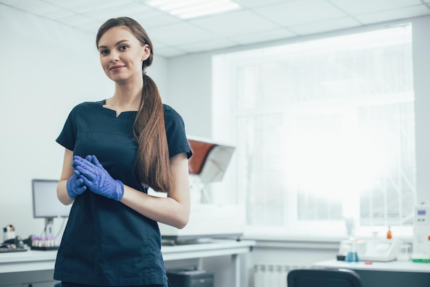 Bella signora allegra in uniforme blu scuro e guanti di gomma in piedi in laboratorio e sorridenti. Banner del sito web