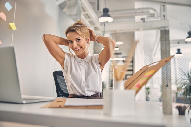 Bella signora bionda che sorride mentre si mette i capelli in ufficio