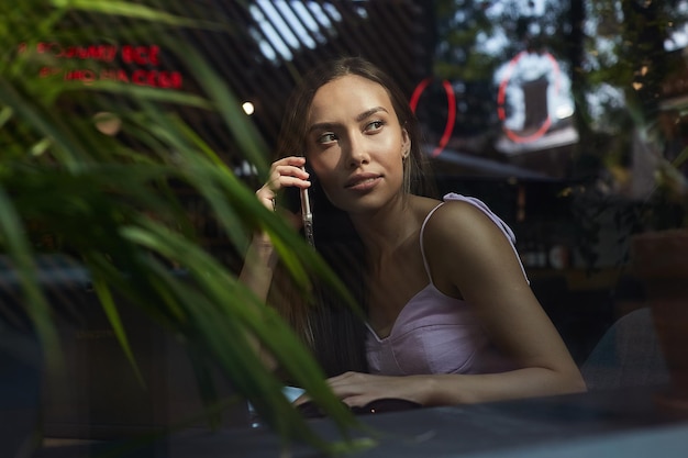 Bella signora che chiama per telefono sparata attraverso il vetro della finestra fuori dal caffè?