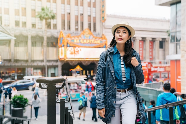 bella signora che sale le scale, facendo shopping durante le vacanze. Stile di vita della donna asiatica in America. ragazza sicura di sé sorridente con cappello e giacca di jeans.