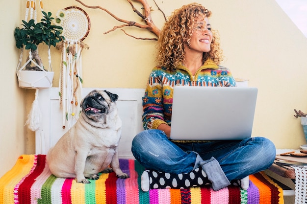 bella signora di mezza età capelli ricci lavora con un laptop all'aperto a casa in terrazza sorridendo e guardando al suo fianco