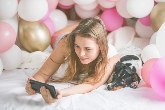Bella signora in pigiama che fa selfie nella sua camera da letto usando il telefono e abbraccia il suo cane.