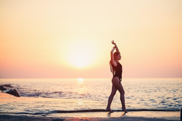 Bella signora in un costume da bagno nero in riva al mare Volto sorridente con un cappello di paglia sulle spalle Luce dorata del tramonto