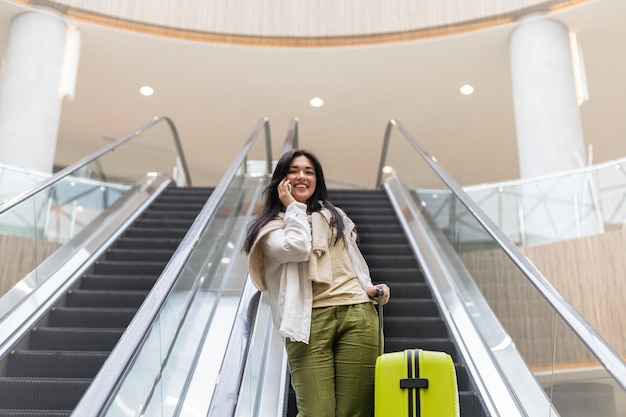 Bella signora turista che scende con i bagagli sulla scala mobile al terminal dell'aeroporto internazionale