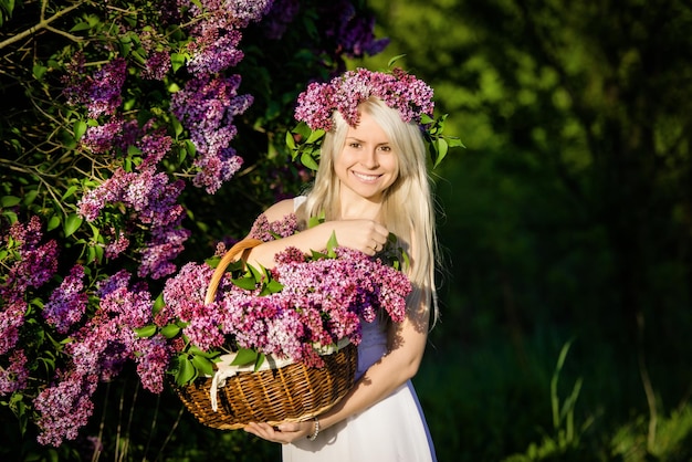 Bella sorridente giovane donna bionda indossa corona e bouquet di fiori lilla nel cestino