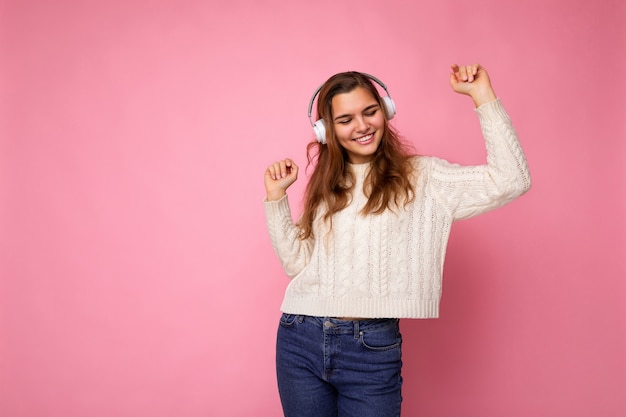 Bella sorridente giovane donna riccia bruna che indossa un maglione bianco isolato su sfondo rosa