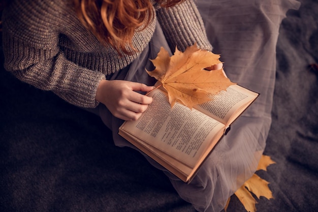 Bella sorridente giovane studentessa seduta e libro di lettura al parco autunnale caduta foglie gialle del fogliame