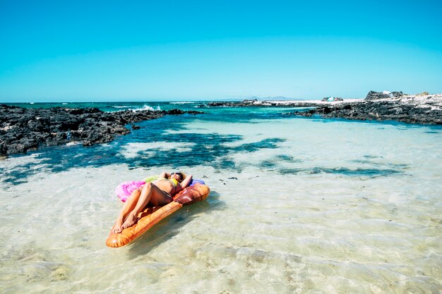 Bella spiaggia e acqua dell'oceano tropicale con una bella donna sdraiata su un materasso gonfiabile colorato lilo rilassandosi e godendosi la natura del mare e la spiaggia durante le vacanze estive