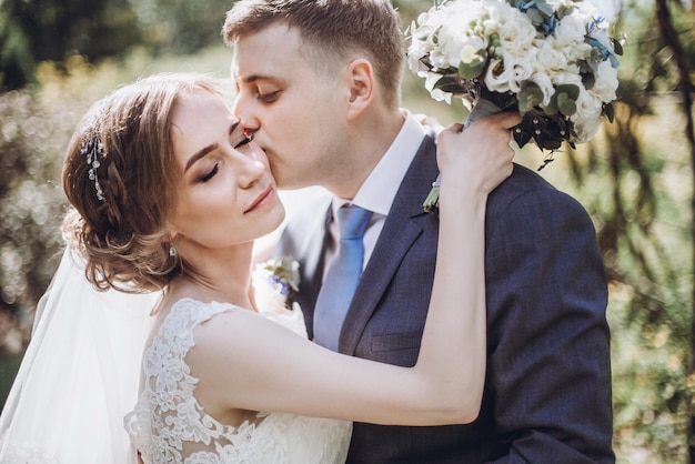 Bella splendida sposa e sposo che si baciano nel soleggiato parco primaverile e si godono il giorno felice coppia di sposi che si rilassa nel verde giardino felice matrimonio momenti concetto di fuga