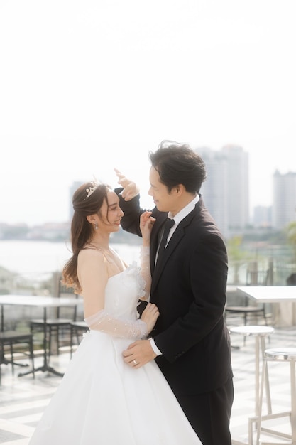 Bella sposa asiatica guardando il suo sposo si sente innamorato sul tetto di un romantico hotel all'aperto Bella coppia in abito da sposa