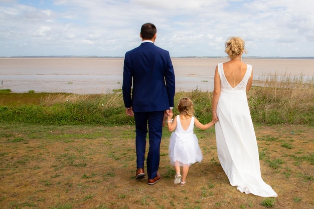 Bella sposa bambino ragazza e sposo nella vista posteriore nel giorno del matrimonio sulla natura verde a parte il fiume