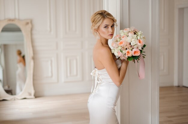 Bella sposa bionda in elegante abito bianco in possesso di un bouquet da sposa