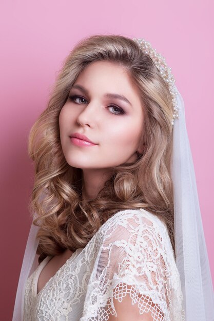 Bella sposa con acconciatura da sposa alla moda e trucco su sfondo rosa