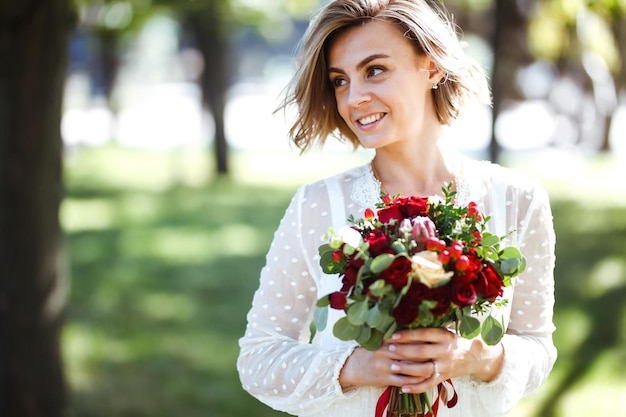 Bella sposa con bouquet da sposa nel parco Donna elegante con trucco professionale e stile di capelli