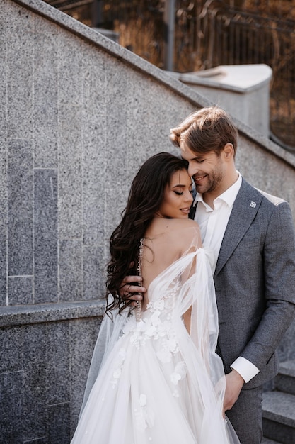 Bella sposa con bouquet moderno che abbraccia con lo sposo elegante nel parco estivo.