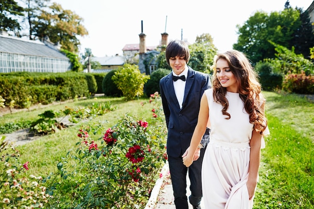 Bella sposa con capelli ricci lunghi e lo sposo in piedi vicino a vicenda al parco verde, bella coppia, giorno del matrimonio.