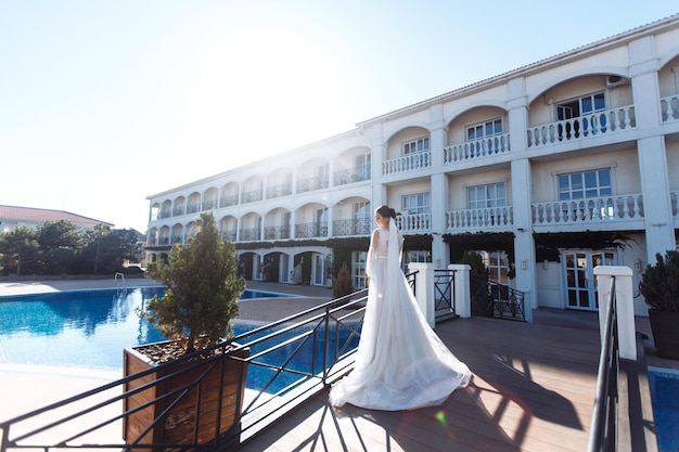 Bella sposa con capelli scuri in lussuoso abito da sposa in posa in balcone con vista mare